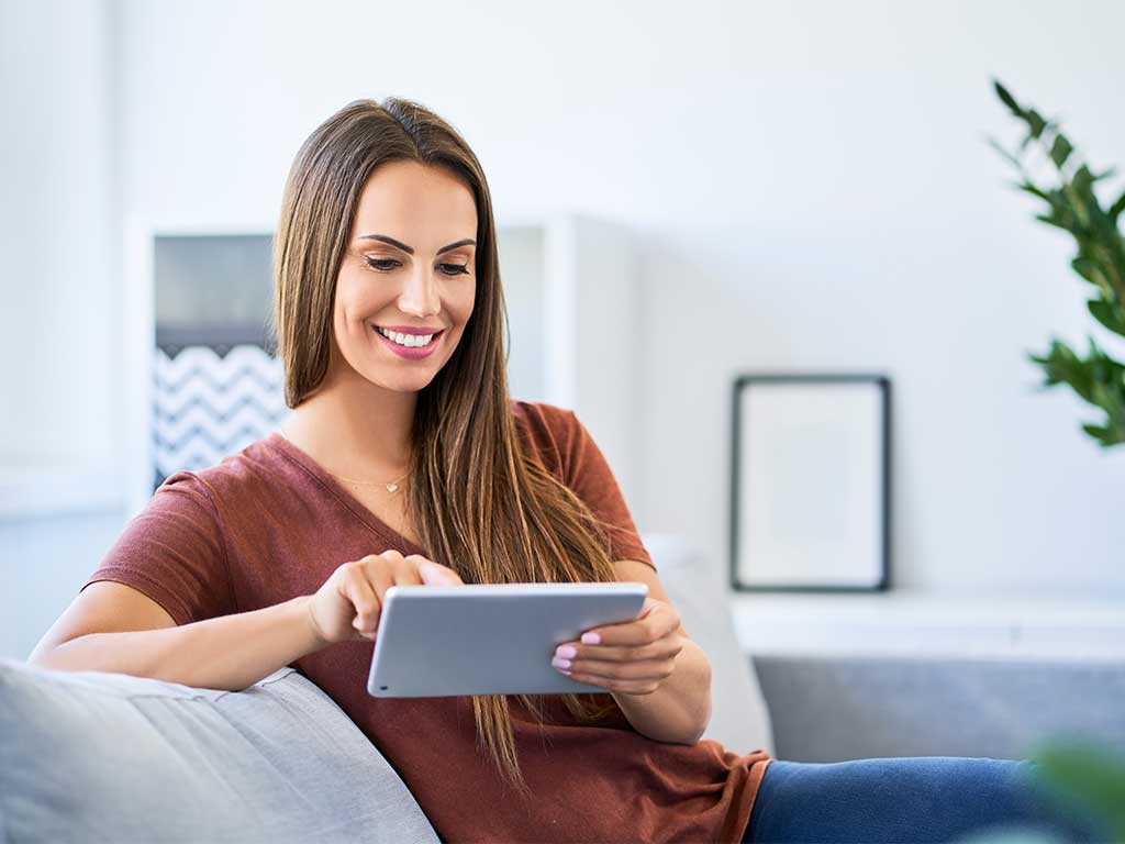 Woman sitting on a couch smiling at ipad
