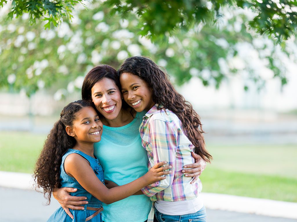 Mom with two daughters hugging and smiling at the camera